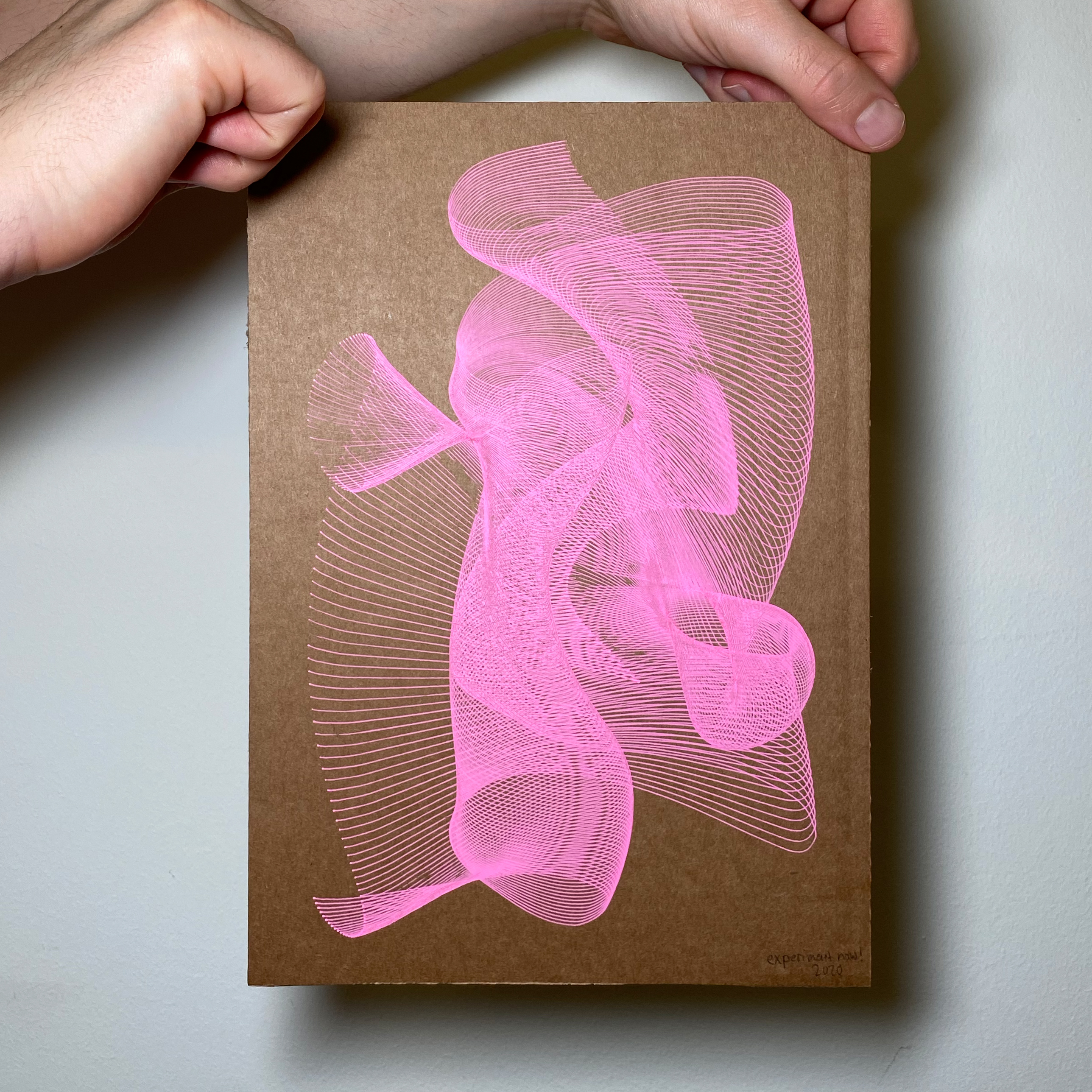 Two hands are holding a used cardboard in the size of A4 with neon pink abstract lines on it.