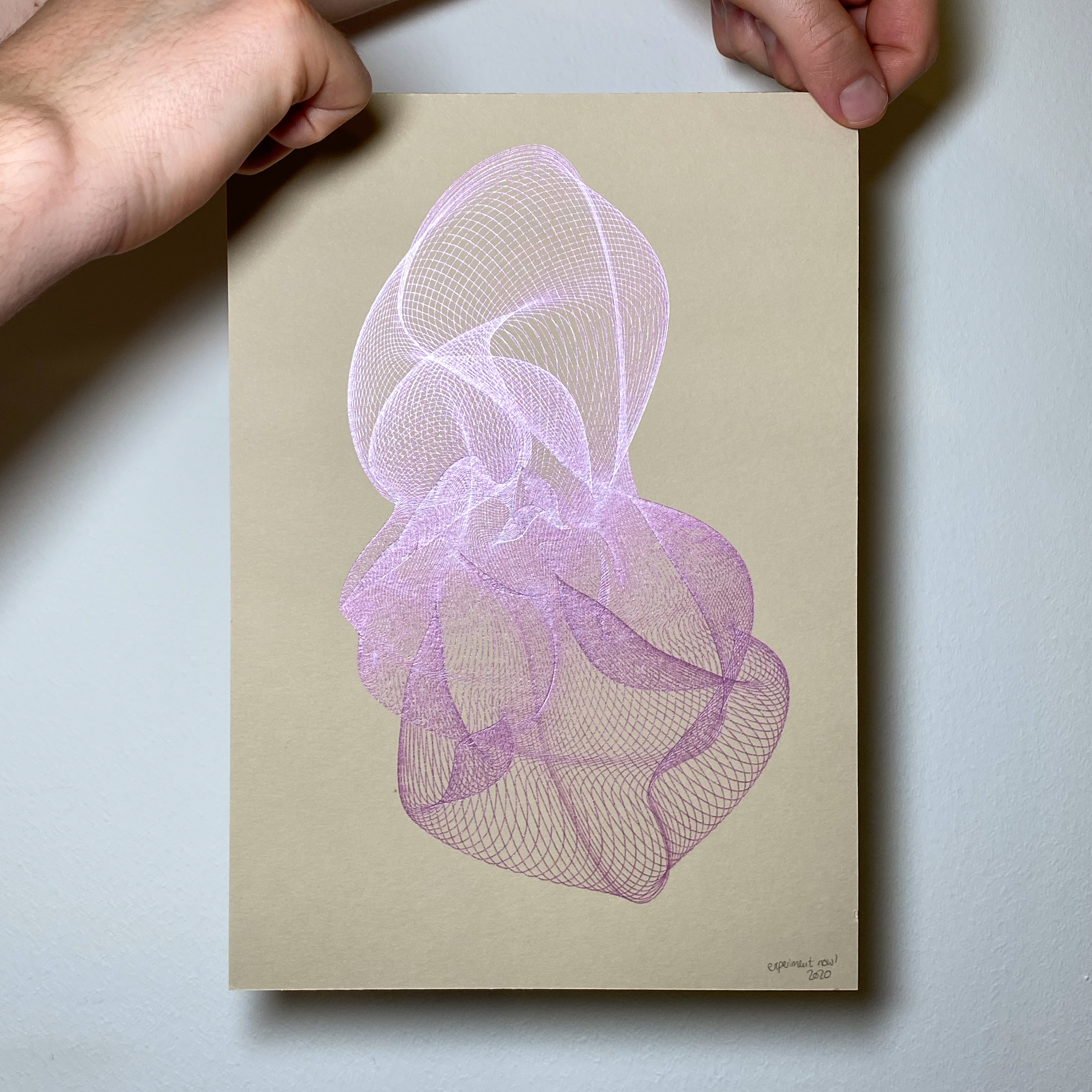 Two hands are holding a beige page (size: A4) with generative art in metallic pink on it.